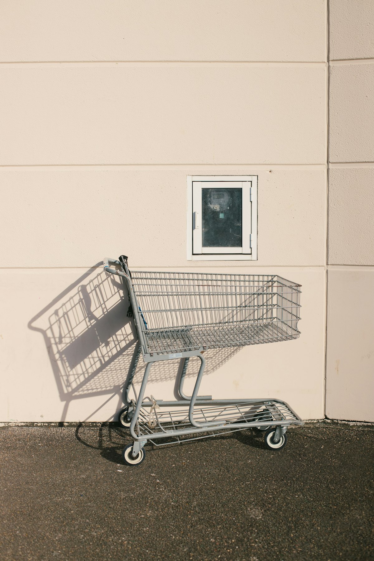 A shopping cart casting a long shadow against a wall