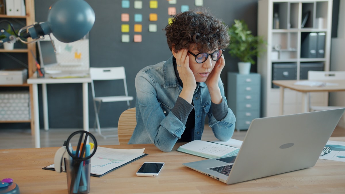 Person looking stressed at a laptop in an office