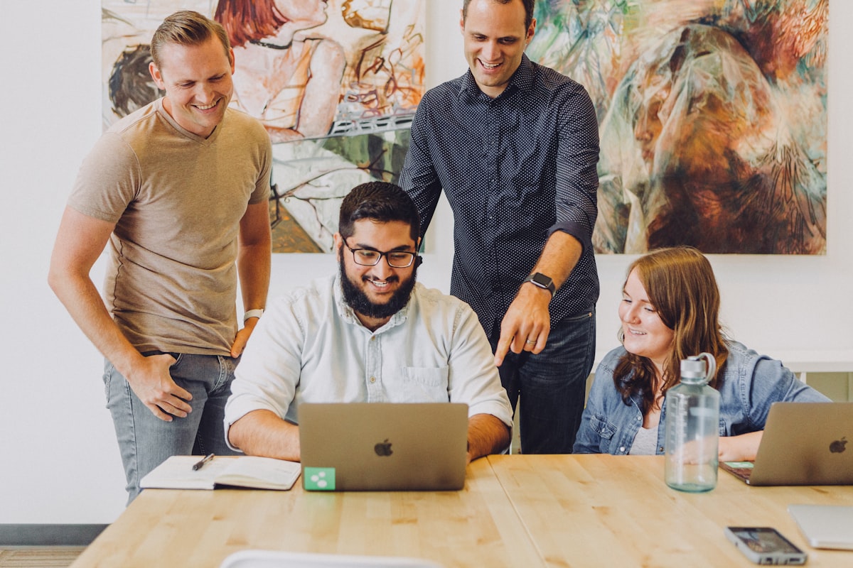 Four coworkers smiling around a laptop at a table